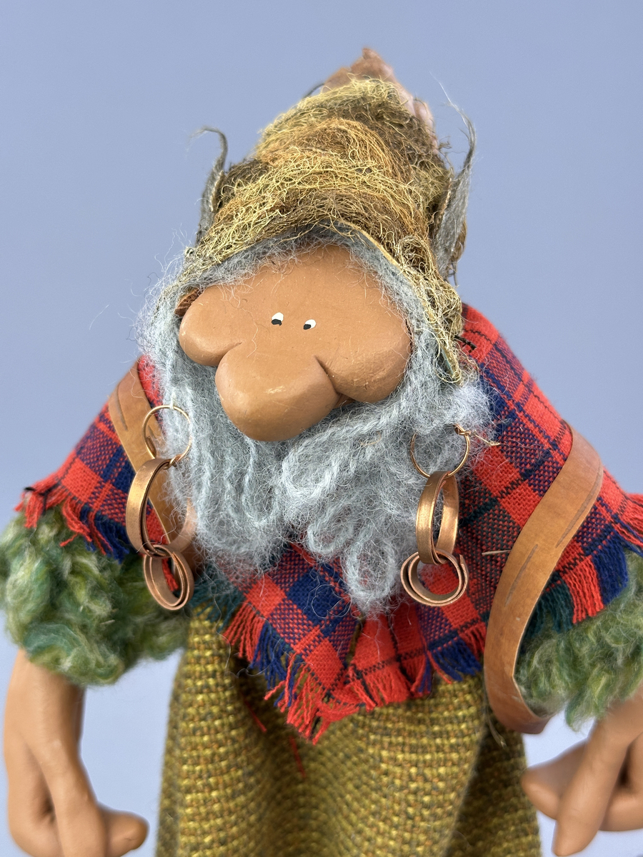 En trollgumma med näverkont på ryggen. Kläder av tyg, skor och mössa av lav och kottfjäll.