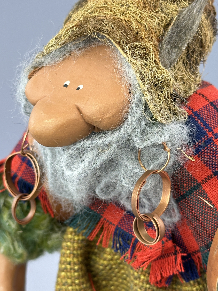 En trollgumma med näverkont på ryggen. Kläder av tyg, skor och mössa av lav och kottfjäll.