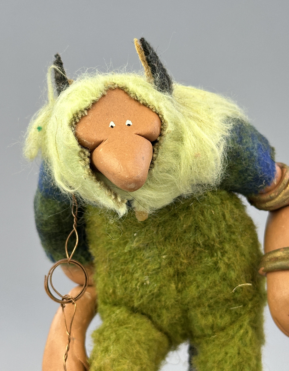 En krokig trollgubbe med böjda knän och rygg. Har lavklädda skor, koppar-örhänge och "guld" ringar på armarna. Är klädd i gröna byxor och blågrön skjorta.



