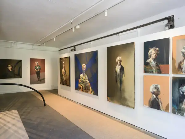 Malerier av Håkon Gullvåg i Galleri Østfløyen på Bogstad Gård, med portretter av personer i ulike positurer og fargerike bakgrunner. Bildene henger i en lys utstillingssal med hvite vegger.