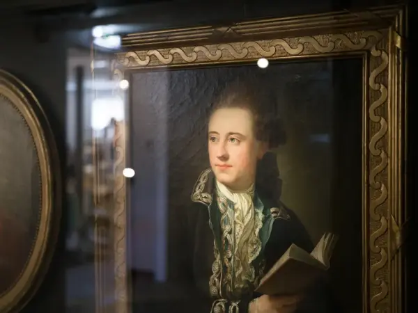 Portrett av Bernt Anker, malt av Jens Juel, i rikt dekorert ramme. Han ser til siden, kledd i mørk jakke med brodert krage og holder en bok.