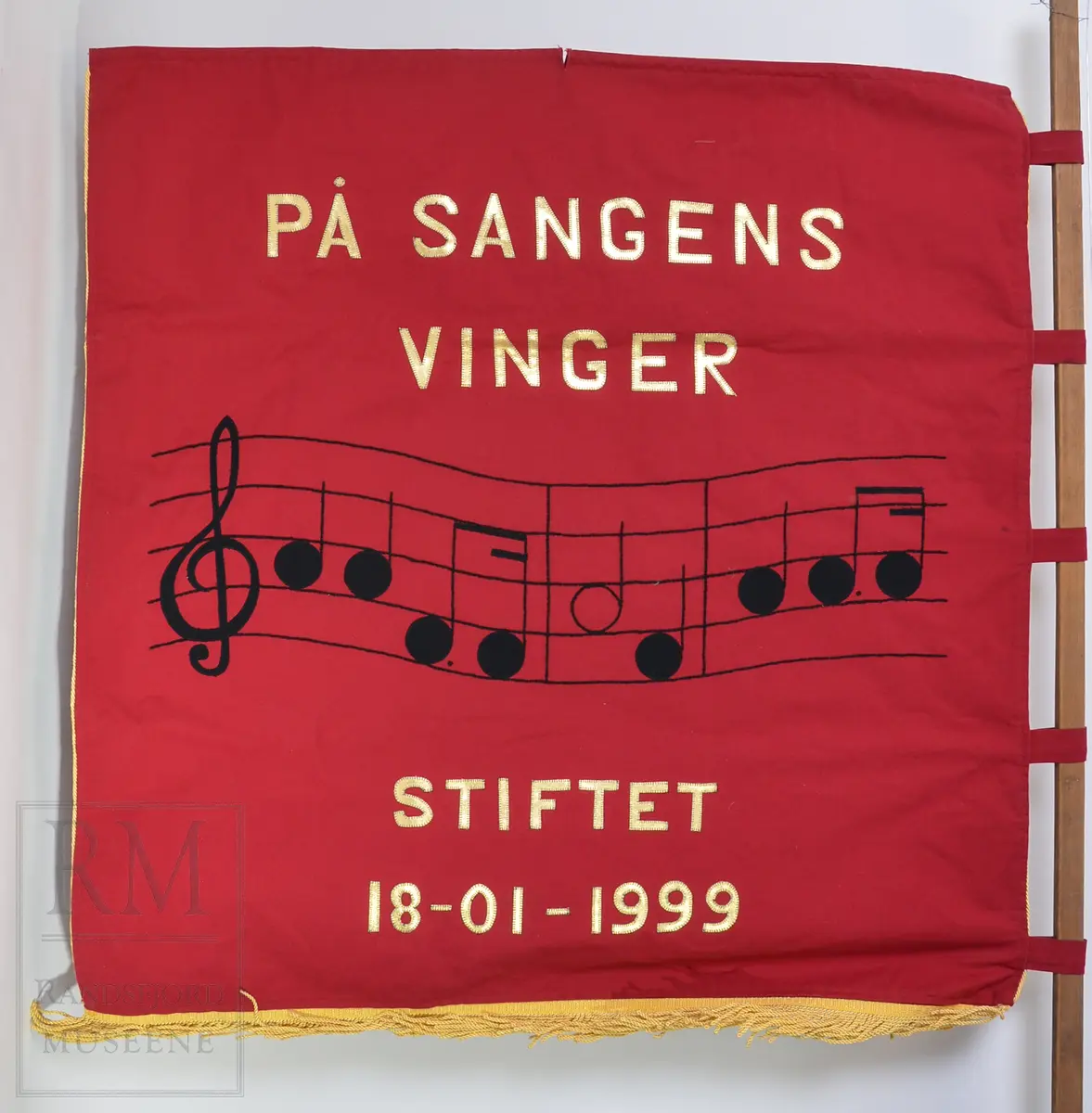 Rød bomullsfane med quiltet motiv
a: fane
b: stangpryd (harpe i messing)
c: bardunsnor m dusker
d: styresnor med håndgrep
e-g: stang og oppheng (e) i alu og messing
h: hvit lærsele
i: bæreveske/ oppbevaringspose i grått kunstskinn