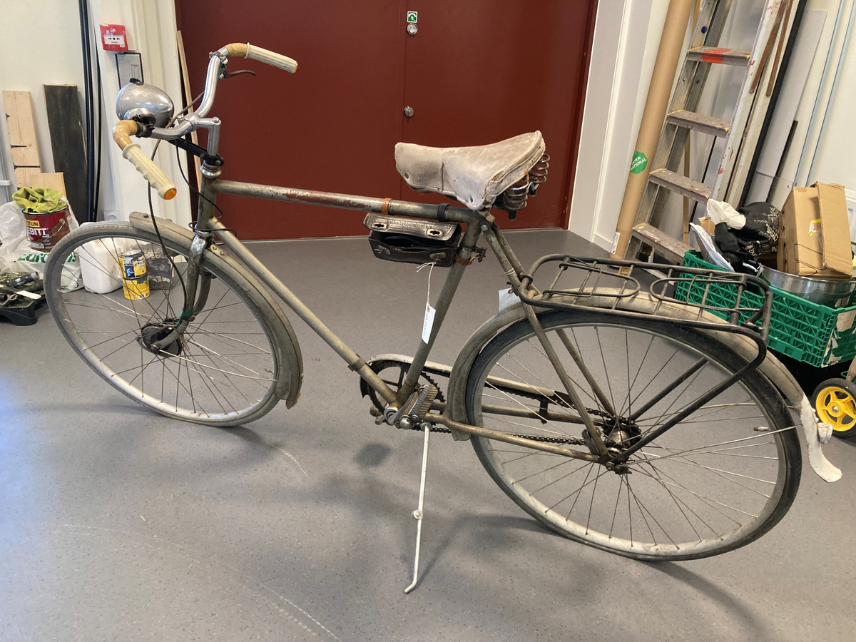 Herresykkel i metall, med sete av lær, lykt og bjelle. Påmontert verktøyeske i lær ved sete. Festet ved bagasjebrett 2 rødmalte halvsirkelformede kasser i tre, med en brannslange i hver.