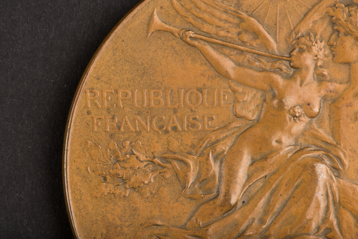 Åtsidan: en man lagerkrönande en kvinna, inskription: EXPOSITION UNIVERSELLE 1889.
Frånsidan: en kvinna blåsande trumpet framför Napoleons byst, inskription: REPUBLIQUE FRANCAISE.
