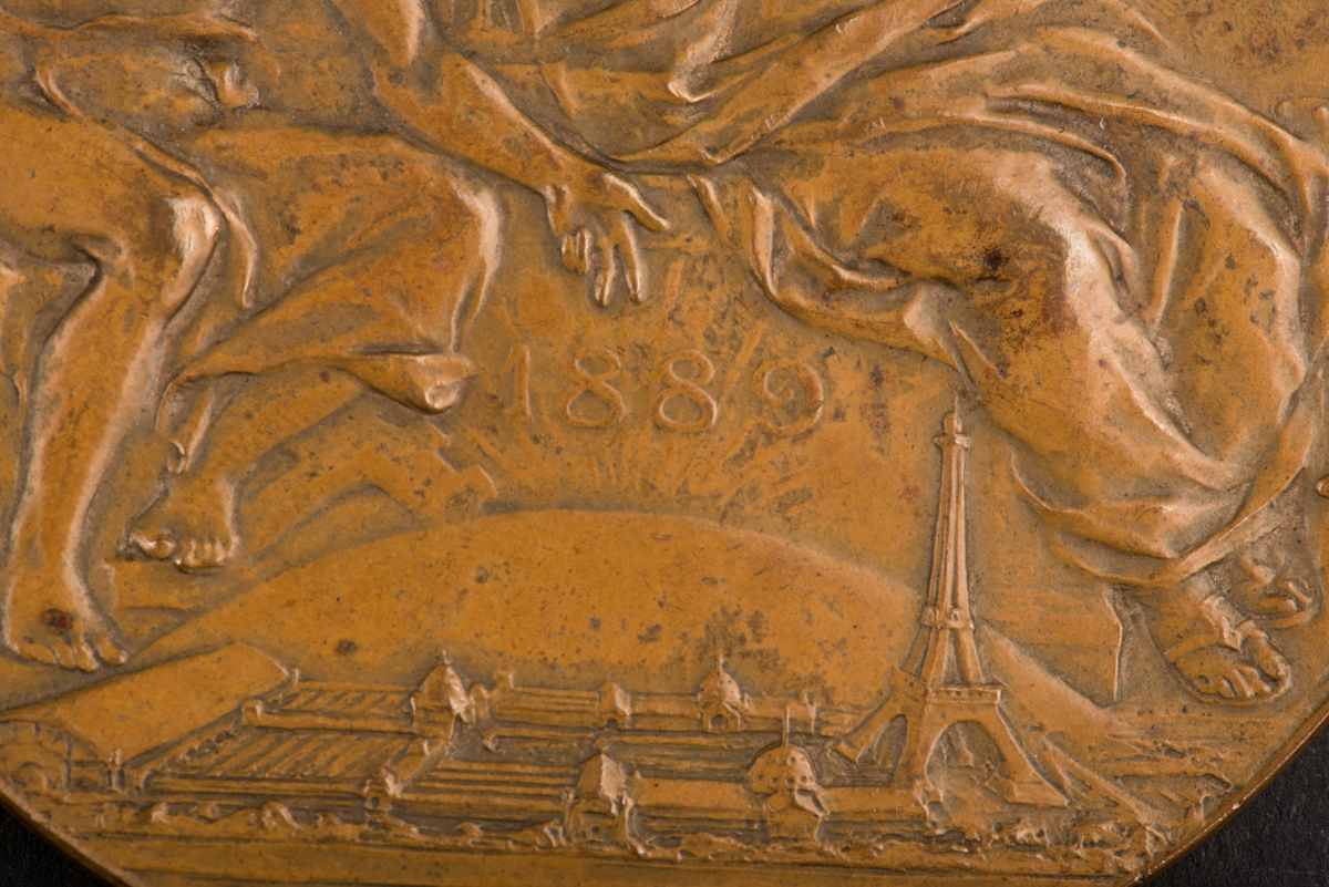 Åtsidan: en man lagerkrönande en kvinna, inskription: EXPOSITION UNIVERSELLE 1889.
Frånsidan: en kvinna blåsande trumpet framför Napoleons byst, inskription: REPUBLIQUE FRANCAISE.