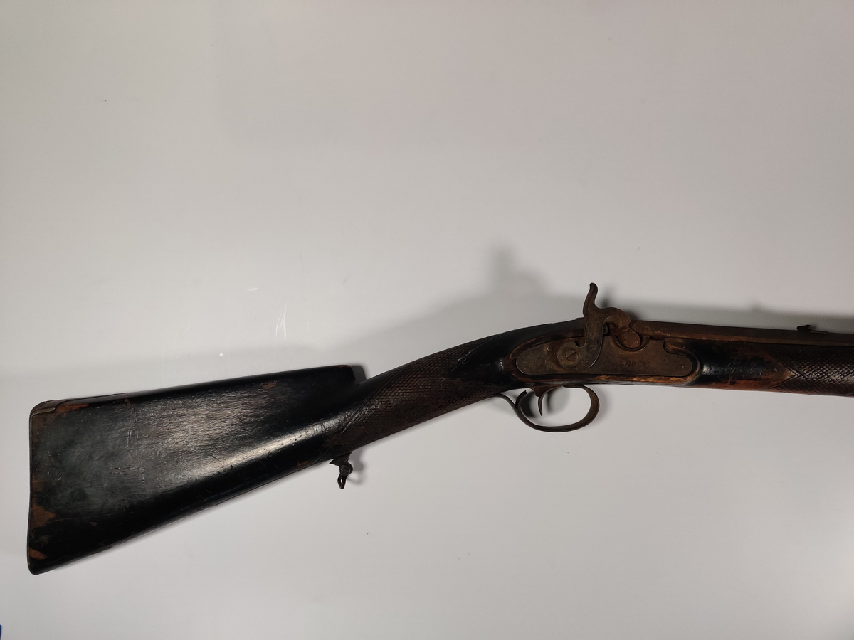 Jaktrifle med perkusjonslås, trolig ombygd fra flintlås. 

Riflet åttekantet løp. Pipa er åttekantet, med dekor og inskripsjon på pipas nedre del, foran skursiktet. Nettingskjært og svartmalt kolbe/skjefte. Hane, lås og beslag dekorert. Ladestokk i tre.