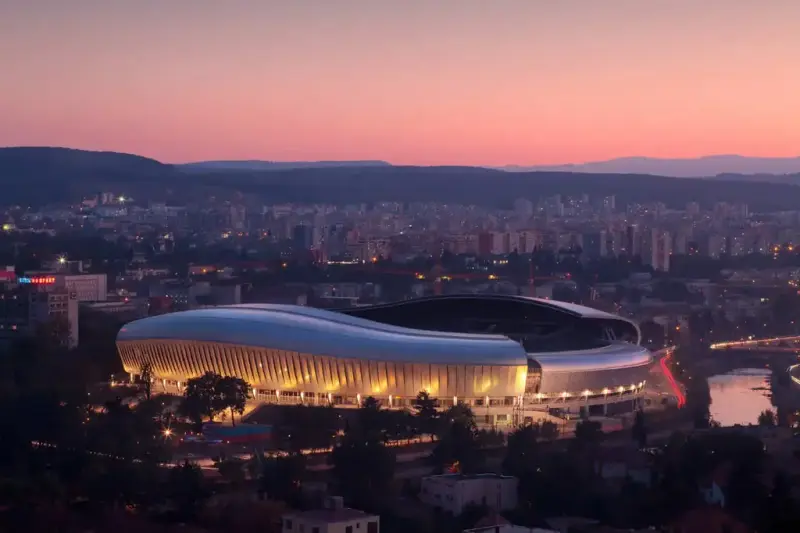 Viser en fotballstadium i Romania. Bygget i aluminium er formet nesten som en bølge og er lyst opp nedenifra. Det skiller seg godt ut i bybildet, ellers dominert av høyblokker.
