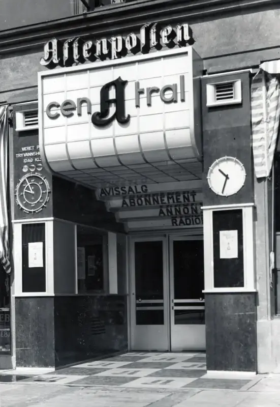 Viser et svarthvitt bilde av en blokk-aktig inngang, med et skilt som danner "terrasser" innover mot selve døren og lager en dybde-effekt til inngangen. Skiltet viser til Central A, hvor A-en står midstilt og i kontrast med Cen - Tral. "plattformene" viser: Avissalg, Abonnement, Annon-*kuttet av* og Radio.  