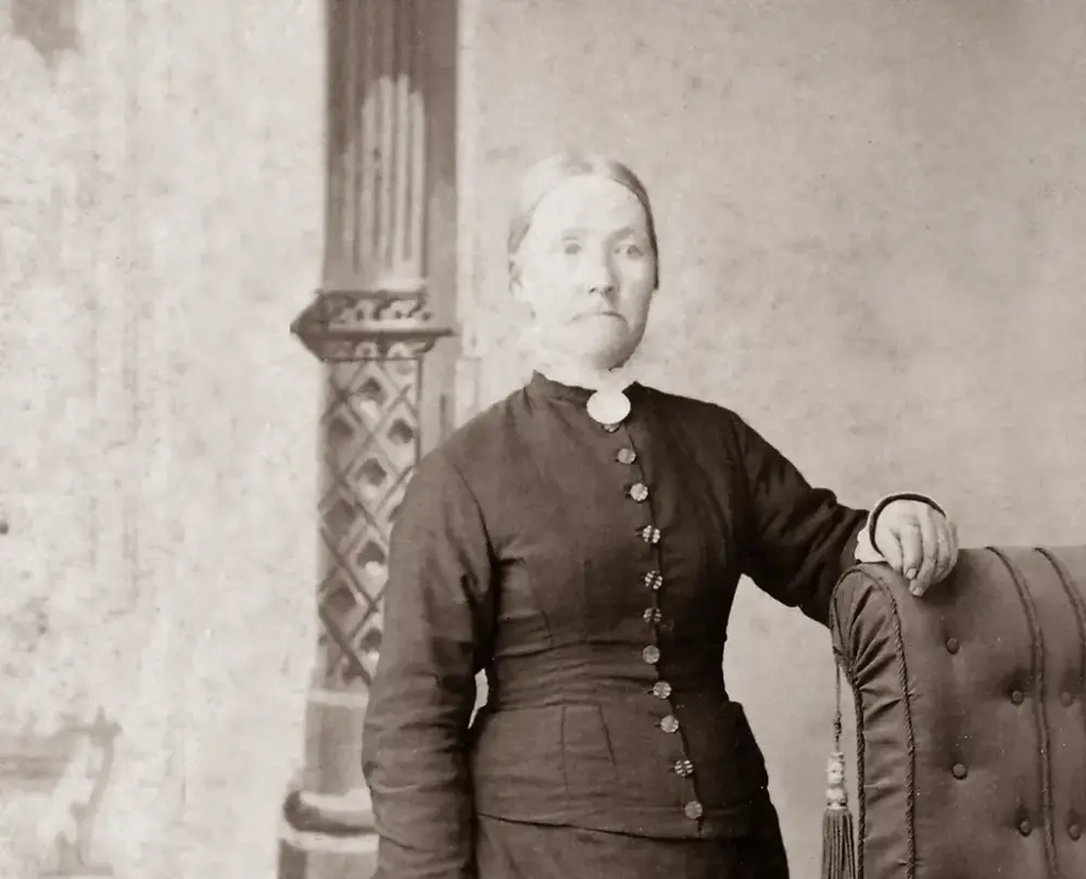 Historisk studioportrett av en voksen kvinne som hviler venstre arm på en stol.