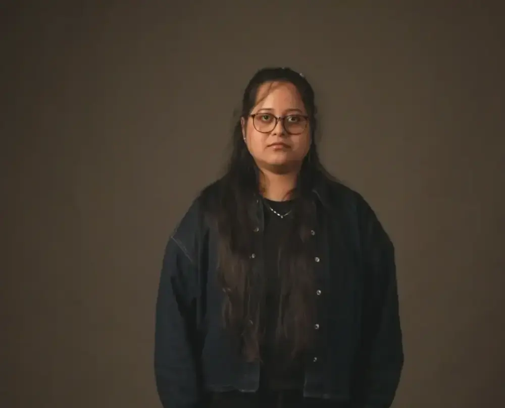 Portrett av en kvinne med mørkt hår og briller. Brun bakgrunn.