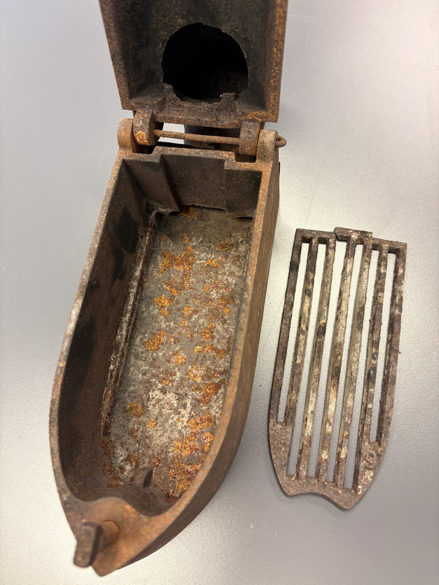 Båtformet strykejern av støpejern. Hengslet lokk med trehåndtak og pipe.