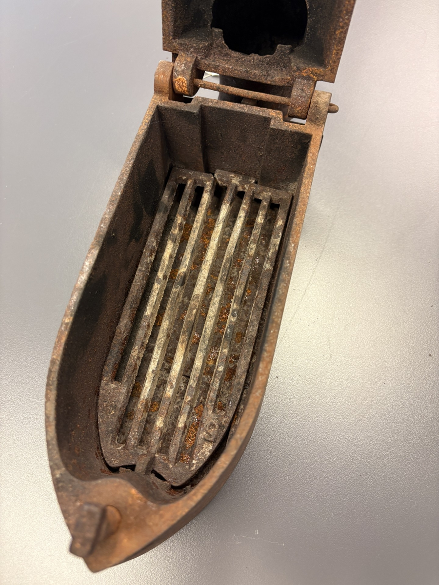 Båtformet strykejern av støpejern. Hengslet lokk med trehåndtak og pipe.