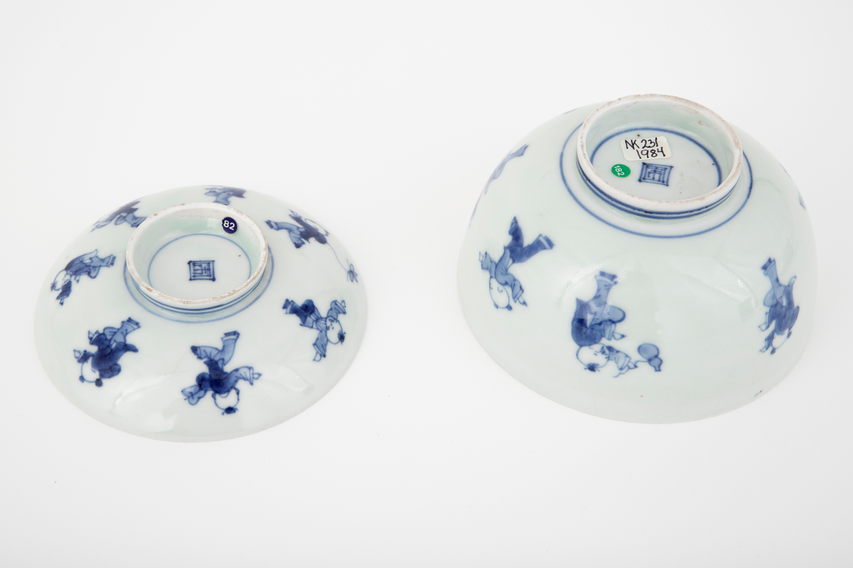 Porselensbolle med lokk med opphøyet midtparti i bunnen av bollen og lokket. Lokket har en diameter som er mindre enn bollens åpning slik at den plasserer seg ca. 1 cm ned i bollen. Lokkets håndtak er utformet som en fotring og kan derfor snus og fungere som en lav skål. Dekket med en hvit glasur og dekorert med en koboltblå underglasur. Bollens og lokkets utside er dekorert med et motiv som forestiller sju lekende barn. På innsiden er de dekorert med et motiv som forestiller to lekende barn samt en geometrisk bord langs kanten.