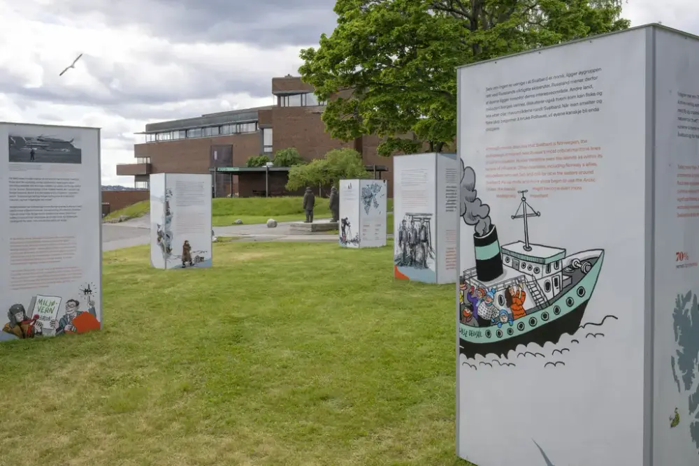 Flere høye, hvite informasjonssøyler med Svalbard‑illustrasjoner står på gress foran museumsbygning.