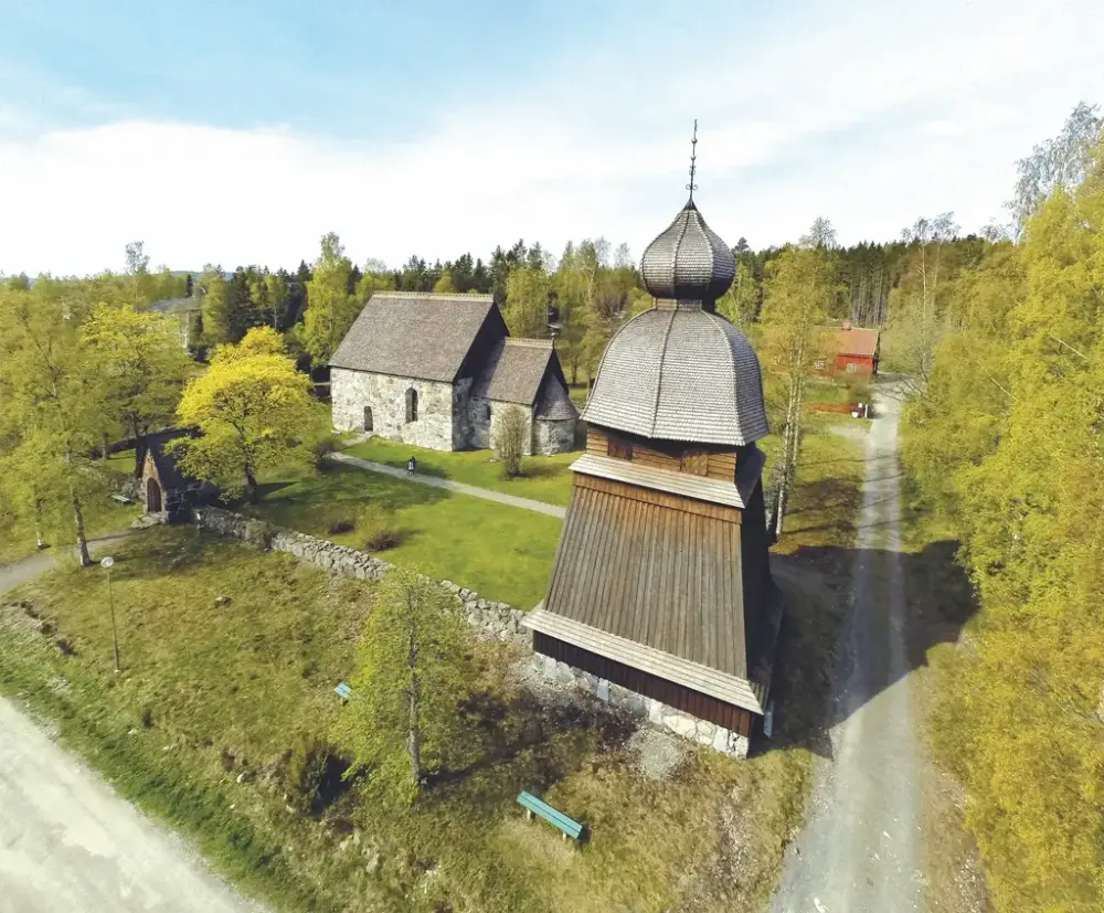 Klockstapel och kyrka med stenmur i grönska.