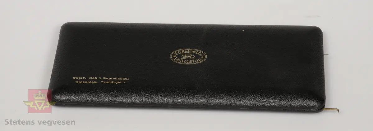 Passersett i etui, består av atten deler (en del mangler). Etuiet består av sort skinntrukket treverk og har fløyelsbelagt innside i svart farge. Produsentens logo inne i lokket.
