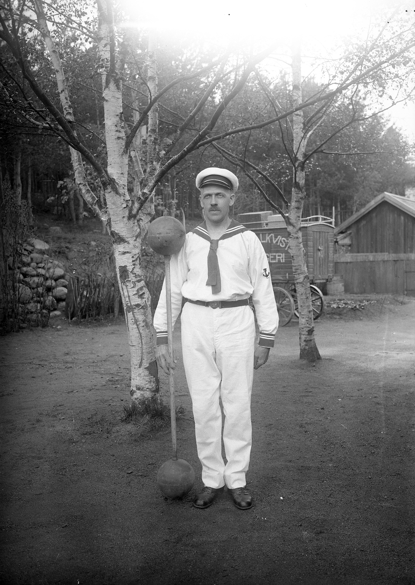 Man ifrån atletklubben Heros klädd i sjömanskostym poserar bredvid viktstång utomhus tidigt 1900-tal.