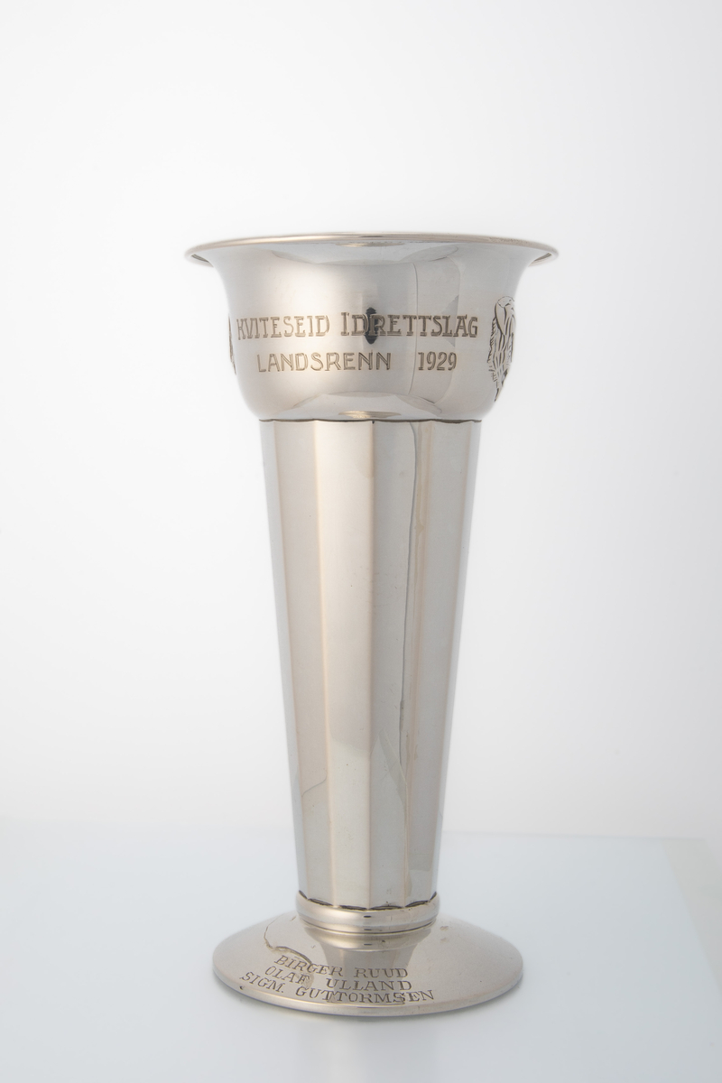 Sølvpokal med mangekanta form på hoveddelen, låg stett og motiv og innskrift på øvre del. Motiv av hovudet til ein tiger (Tiedemanns tobakk logo).