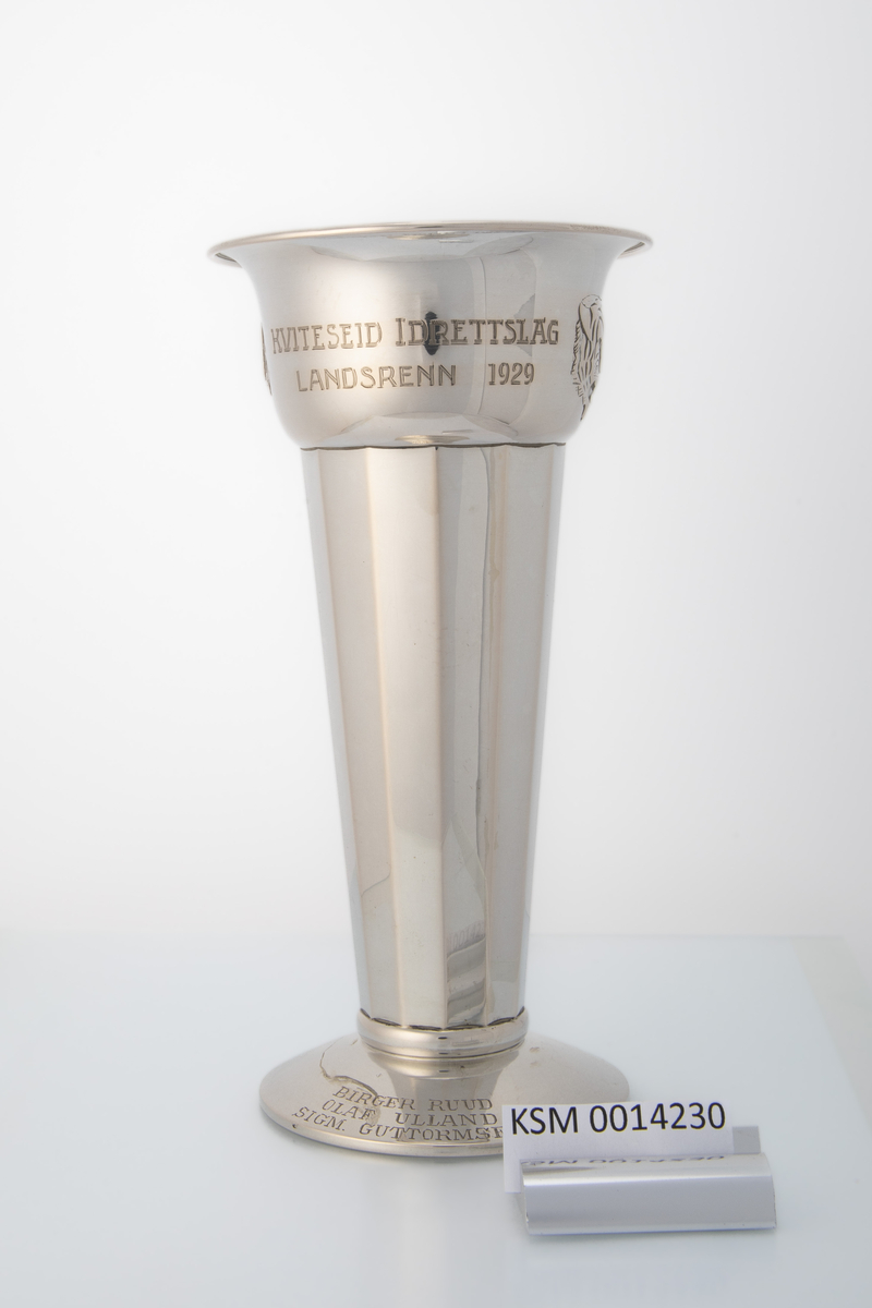 Sølvpokal med mangekanta form på hoveddelen, låg stett og motiv og innskrift på øvre del. Motiv av hovudet til ein tiger (Tiedemanns tobakk logo).