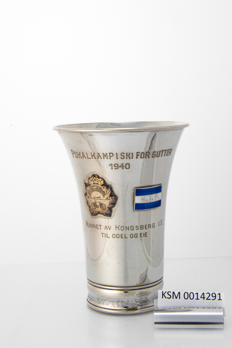Enkel pokal uten stett, med to emblem (Kongsberg IF og N.I.F) og inskripsjon.