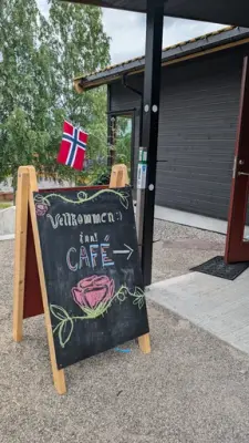 Bilde av inngangen på solbakken kafe med skilt. Skiltet er svart og det er skrevet og tegnet en rose med kritt "Velkommen inn - Cafe"