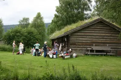 Bilde av målstua på Trysil bygdetun med en gruppe mennesker utenfor. De holder på med ulike husflidsaktiviteter. 