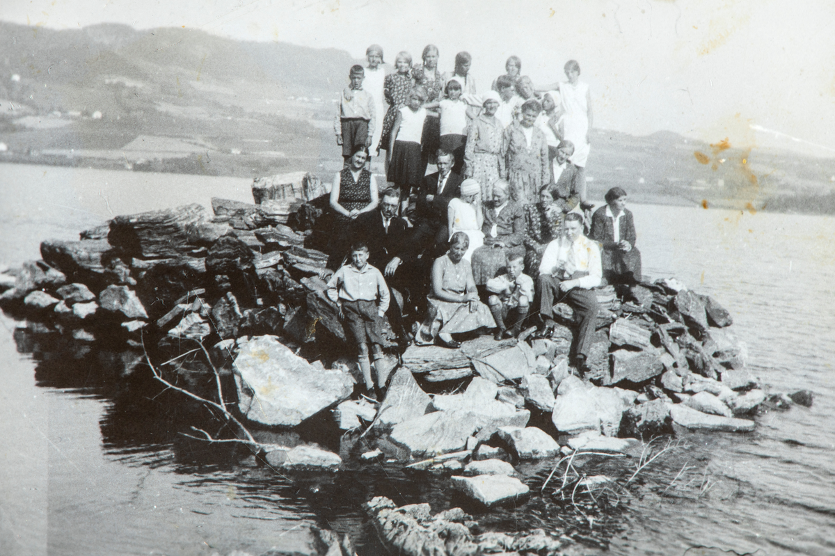 Gruppe mennesker sittende på Skjæra med Espa i bakgrunnen. På bakerste rad fra høyre Inger Løvstad og Ingrid Brodal. Til høyre, på første rad sitter Lars O. Holm, bak ham kona Helma Holm. I midten på rad 2 sitter Inga Løvstad og datteren Borghild. Trolig er det Ingas mann, Syver, rett bak henne. Til høyre på rad 3, Berta Brodal. 1930-tallet.