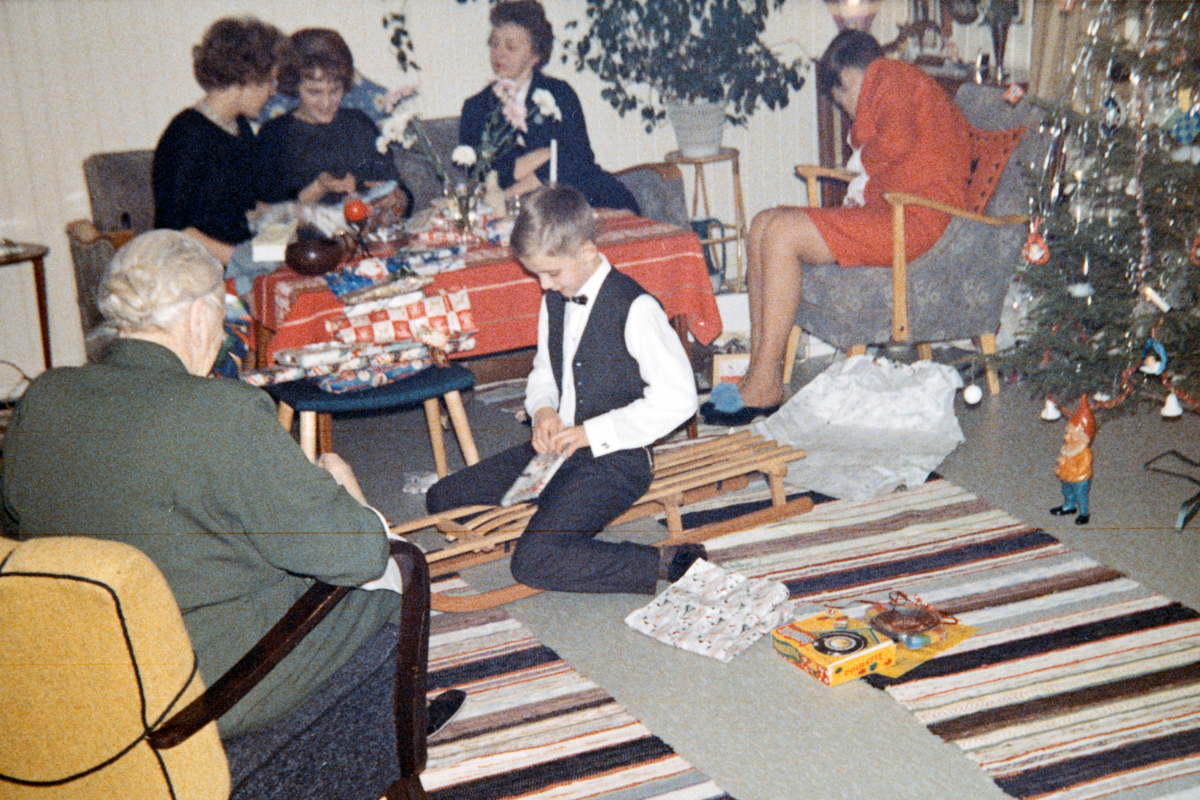 Stig Erik Nordnes sitter på gulvet, og åpner julegaver. Juleaften 1962/63. Løvstad, Espa. Inga Løvstad (med ryggen til). Bjørg Nordnes (gift Midtlund), Eva Nordnes (gift Barmoen), Inger Gundersen, Ruth Gundersen (gift Nordnes).