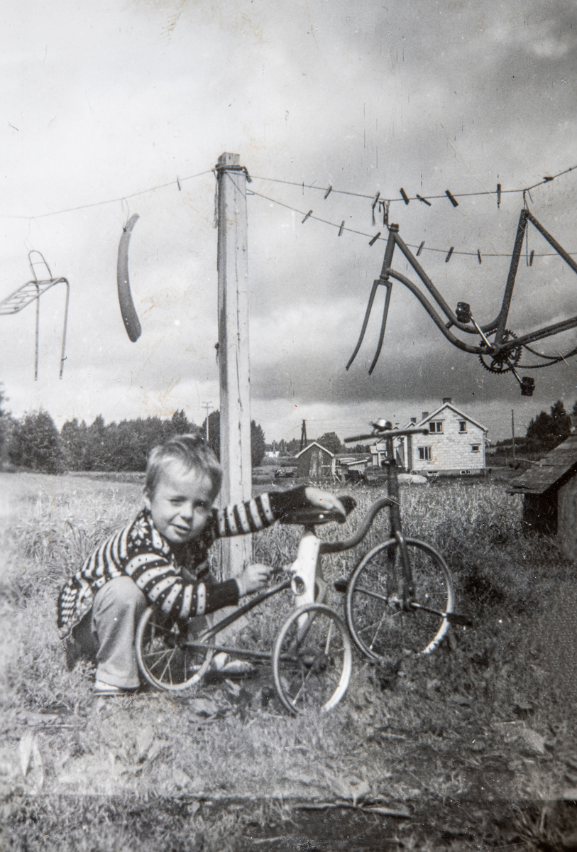 Svein Fjeld Løvstad med trehjulssykkelen sin. Diverse sykkeldeler henger til tørk i bakgrunn. Stange, 1954/55.