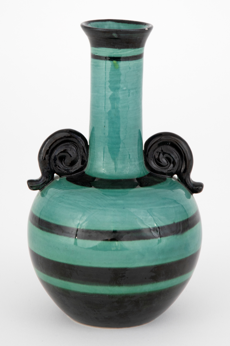 Vase i fajanse. Kuleformet korpus med en lang, smal hals og en svak, utoverbrettet munning. Spiralformede hanker der korpus går over til hals. Vasen er glasert med en blank, grønn glasur. Dekorert med horisontale, svarte striper i forskjellige tykkelser. Tett, finkornet hvitt gods.