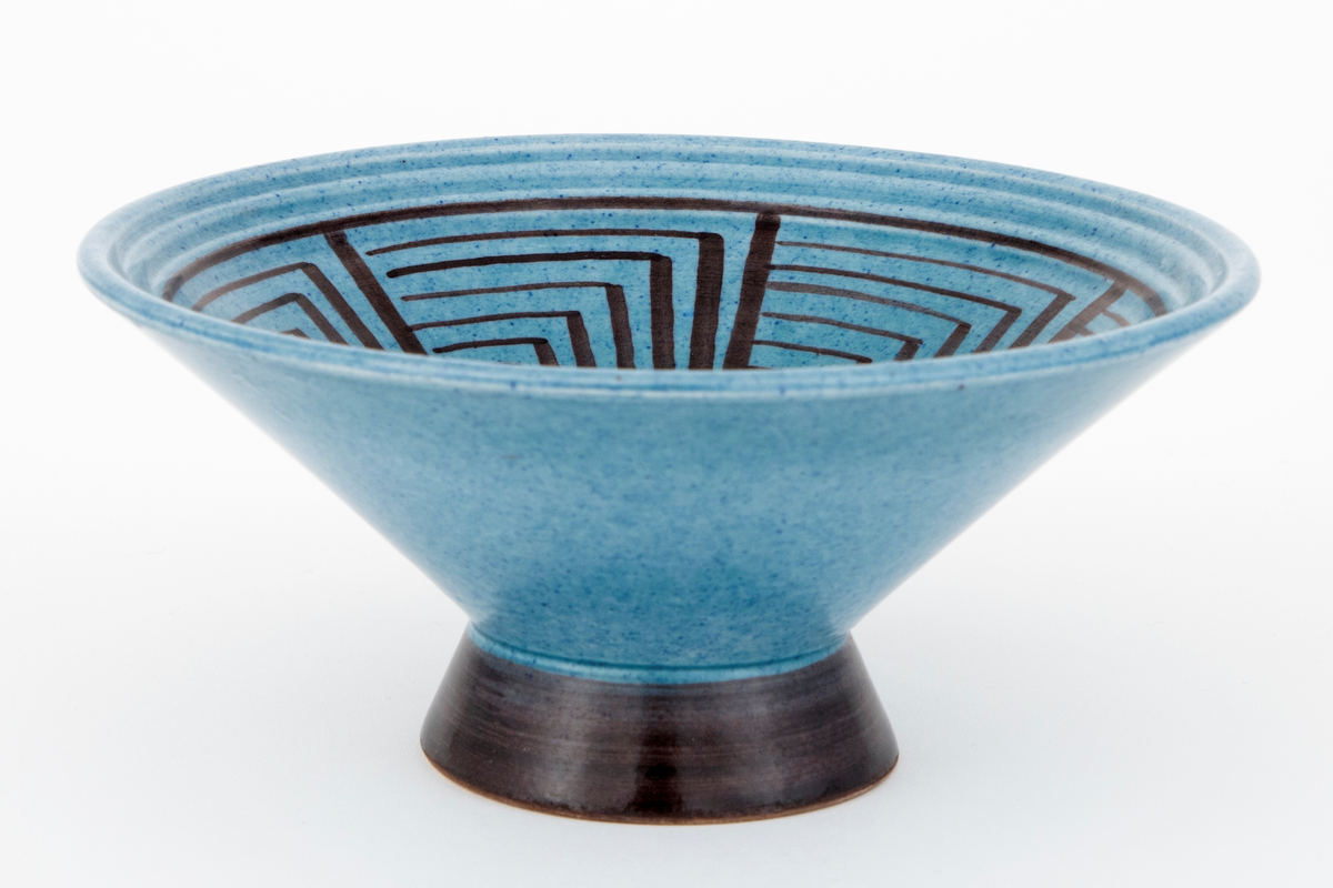 Skål i fajanse. Konkav fot og kjegleformet korpus. Skålen er glasert med en blank, blå glasur. Foten er glasert med en blank, svart glasur. Innsiden er dekorert med et geometrisk mønster i svart. Tett, finkornet hvitt gods.