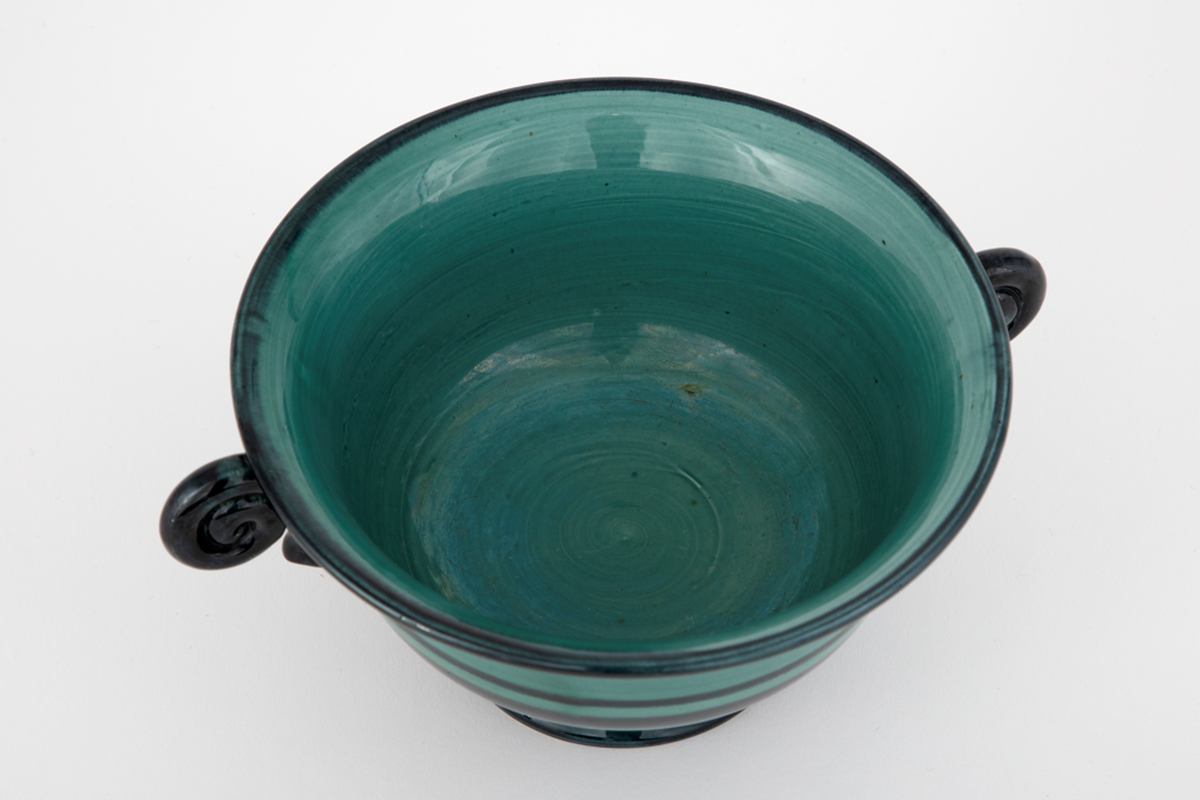 Vase i fajanse. Konkav fot, rund korpus, svakt utoverbrettet kant samt spiralformede hanker. Vasen er glasert med en blank, grønn glasur. Dekorert med horisontale, svarte ringer i forskjellige tykkelser. Hankene er glasert med en blank, svart glasur. Tett, finkornet hvitt gods.