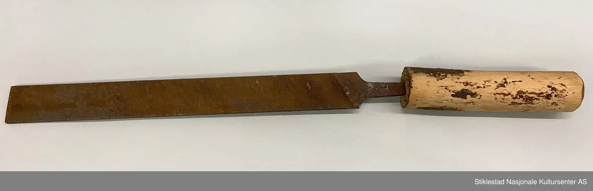Fabrikkprodusert metallfil med skråstilte filspor, enkelthogd på begge sider. Montert på et kort treskaft. Skaftet er saget i passe lengde og barket. Mye rust