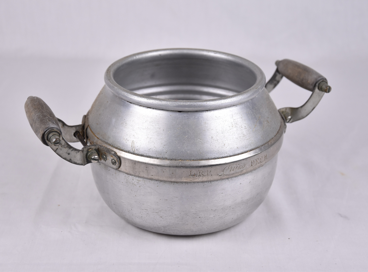 Kjele i aluminium med trehank på hver side. I midjebåndet er det stemplet D.R.P.  og D.R.G.M. og varemnerket Fruco.