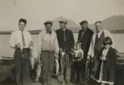 Fem menn og to barn står og viser fram fiskefangsten i Bogøy i Steigen. Fra venstre: Ukjent, Arne Stensland, Ragnar Bogen, Jacob Bogen og Hans Stensland. Gutten er Ragnars sønn Roald Bogen.