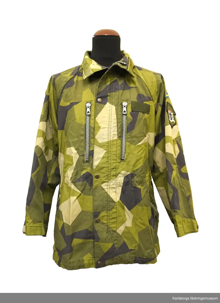 Jacka m/1990 är sydd i kamouflagetryckt varpsatin av bomull samt polyester. Fältjackans ärmar och rygg är skurna i ett stycke, med sömn mitt på ryggen. Ärm och framstycke möts i reglansömn. I nederkanten och i midjan finns snören för reglering av vidden. Yttertyg och foder bildar fickor till två bröstfickor och två sidfickor med blixtlås. Jackan stängs framtill, med ett tvåvägs öppningsbart blixtlås som täcks av ett vindskydd utrustat med tryckknappar. På kragen finns märke för överstelöjtnant på vänster sida samt ett märke för kavalleriet på höger sida. På vänster arm ett livregementets husarer-märke. Storlek: 180/75.