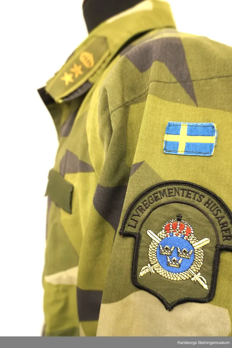 Jacka m/1990 är sydd i kamouflagetryckt varpsatin av bomull samt polyester. Fältjackans ärmar och rygg är skurna i ett stycke, med sömn mitt på ryggen. Ärm och framstycke möts i reglansömn. I nederkanten och i midjan finns snören för reglering av vidden. Yttertyg och foder bildar fickor till två bröstfickor och två sidfickor med blixtlås. Jackan stängs framtill, med ett tvåvägs öppningsbart blixtlås som täcks av ett vindskydd utrustat med tryckknappar. På kragen finns märke för överstelöjtnant på vänster sida samt ett märke för kavalleriet på höger sida. På vänster arm ett livregementets husarer-märke. Storlek: 180/75.