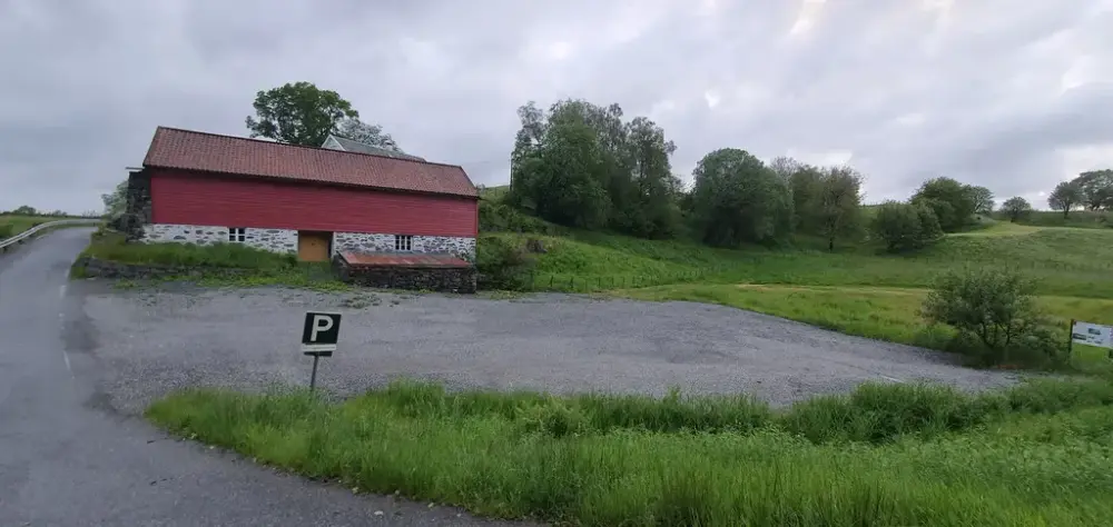 Parkeringsplassen ved Fosseløa, ei raud løe med steinmur og bølgjeblikk på taket. 