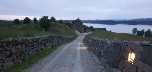 Grusveg ned til informasjonsbygget med steingard på kvar side. Bildet er tatt ein sein sommarkveld.