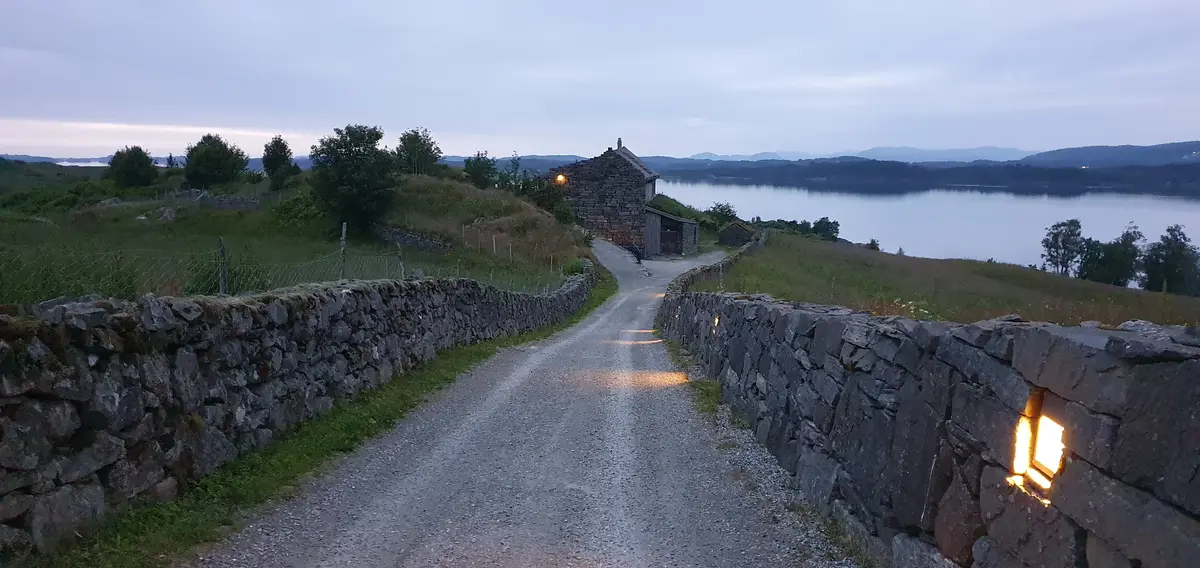 Grusveg ned til informasjonsbygget med steingard på kvar side. Bildet er tatt ein sein sommarkveld.