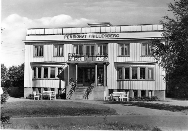 Pensionat Frillesberg, Frillesås. Pensionatet uppfördes 1938 och var ett av badortens åtta pensionat under 1940-talet. Tvåvåningsbyggnaden i trä har en centrerad entré med kolonner som bär upp skärmtaket och välvda burspråk på ömse sidor. Såväl stentrappan som balkong över entrén har smäckra smidesräcken. Takterassen sträcker sig längs takets hela bredd. Nedanför burspråken står trädgårdsmöbler.