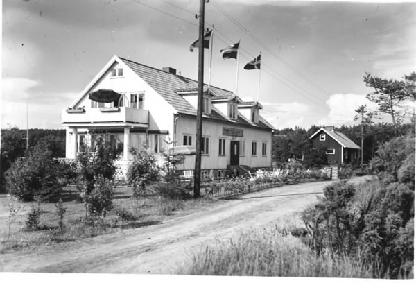 Exteriörbild. Pensionat Västanfläkt, Skreanäs (Ringsegård). Putsad byggnad med sadeltak, tre takkupor och gavelbalkong, uppburen av två kolonner på altanen inunder. På varje takkupa sitter en flaggstång. Byggaden ligger intill vägen, som leder mot havet åt vänster, och omges av en trädgård. Lilly och Bengt Bengtsson lär ha uppfört pensionatet i slutet av 1940-talet och det kallades även för Skreagården.
