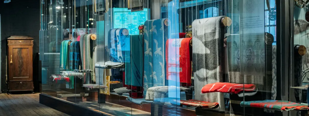 Viser utstilling av mange forskjellige tepper og tekstiler i mange forskjellige farger og mønstre.