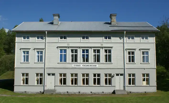 En grå, stor symmetrisk byggnad med många fönster: Styrnäs församlingshem.