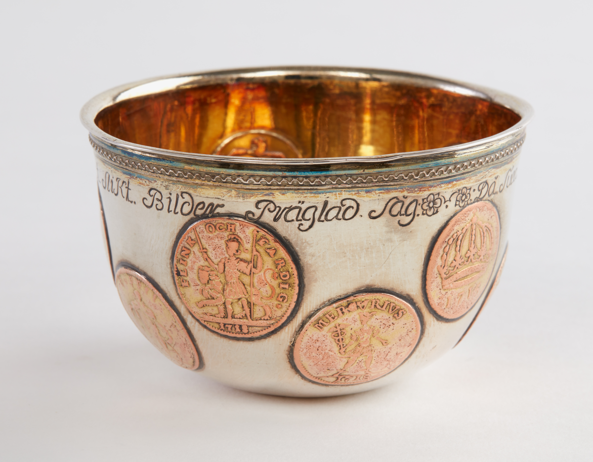 Skål av förgyllt silver. Rundad botten. Smalt utställt bräm. Tio infällda kopparmynt "1 daler silvermynt" med olika motiv. I botten ett infällt silvermynt: "Dominvs protector mevs, X II, 1718". graverat under brämet: "Då Suea Land i Krig och örling diúpat Låg man úppå Kopparmynt Slikt Bilder Präglad Såg". Ostämplad.

Donation 1991 genom testamente efter makarna Tor och Margareta Ärje.