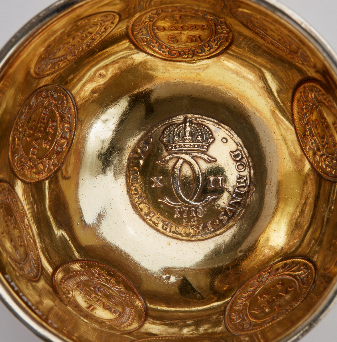 Skål av förgyllt silver. Rundad botten. Smalt utställt bräm. Tio infällda kopparmynt "1 daler silvermynt" med olika motiv. I botten ett infällt silvermynt: "Dominvs protector mevs, X II, 1718". graverat under brämet: "Då Suea Land i Krig och örling diúpat Låg man úppå Kopparmynt Slikt Bilder Präglad Såg". Ostämplad.

Donation 1991 genom testamente efter makarna Tor och Margareta Ärje.