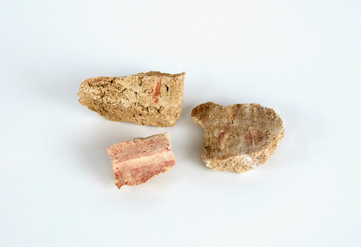 En samling av fragment av målad puts och bruk med kalkputs och bemålning. 17 fyndaskar med fragment i olika storlekar.

Fyndask 1: Totalt 13 fragment med röd och vit färg, en ser ut att ha träavtryck (varit fäst mot ett trästycke).

Fyndask 2: Totalt 7 fragment alla utom en har röd och vit färg, endast en med gråaktig obehandlad puts. 

Fyndask 3: Totalt 1 större fragment med röd och vit färg på enda sidan.

Fyndask 4: Totalt 4 fragment alla utom en med röd och vit färg, endast en med vit puts. 

Fyndask 5: Totalt 3 fragment med röd och vit färg, varav en är sotig. 

Fyndask 6: Totalt 3 fragment med röd och vit färg, en mycket tydlig medan de andra två mer diffusa. 

Fyndask 7:  Totalt 27 fragment, 24 av dessa är bemålade med röd och vit färg, 3  fragment med gråaktig obehandlad puts. 

Fyndask 8: Totalt 5 fragment, varav 4 större och en mycket liten. Alla större fragment med olika karaktär. En med vit kalkbruk och utan putsad yta, en annan med svart och röd putsad yta. Det tredje fragmentet har lite rödfärgad puts bevarad och på andra sidan ser det ut att ha träavtryck (varit fäst mot ett trästycke). Det fjärde fragmentet har en mer brungrå nyans. I fyndasken låg en lapp med text N. om V. portalen. 

Fyndask 9: Totalt 13 fragment, varav ett större fragment med svart och rödmålad puts. Ett annat fragment med svart och vitmålad puts, det tredje fragmentet har endast svartmålad puts. Sedan finns tre rödmålande putsfragment, samt tre fragment med röda linjer. Fyra fragment är ytterst små och intetsägande.

Fyndask 10: Totalt 9 fragment samt smådelar varav två har rött färgfragment. Det största fragmentet samt fyra andra är svart- och rödmålat. Tre putsfragment har röda linjer.
 
Fyndask 11: Totalt 1 fragment med röda linjer samt en mindre del med blågråa linjer. 

Fyndask 12: Totalt 1 fragment med blågrå rundad linje samt samt en mindre punkt eller koncentration nedanför.  

Fyndask 13: Totalt 5 fragment varav två med rödmålad puts. De andra tre har linjer. 

Fyndask 14: Totalt 1 fragment med vit och rödmålad puts, med flertal linjer som eventuellt kan vara del av en bokstav.
 
Fyndask 15: Totalt 1 fragment med vit och svartmålad puts, med flertal linjer som eventuellt kan vara del av en större figur. Ena delen syns en större koncentration som skulle kunna vara en fågel. 

Fyndask 16: Totalt 1 fragment med vit och rödmålad puts, med flertal rundade linjer som eventuellt kan vara del av växtlig dekor.

Fyndask 17: Totalt 1 fragment med rödmålad puts, med en vit linje.