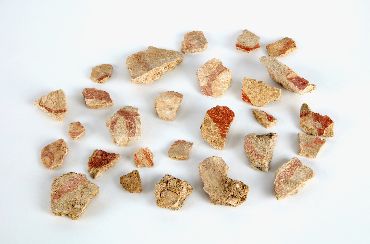 En samling av fragment av målad puts och bruk med kalkputs och bemålning. 17 fyndaskar med fragment i olika storlekar.

Fyndask 1: Totalt 13 fragment med röd och vit färg, en ser ut att ha träavtryck (varit fäst mot ett trästycke).

Fyndask 2: Totalt 7 fragment alla utom en har röd och vit färg, endast en med gråaktig obehandlad puts. 

Fyndask 3: Totalt 1 större fragment med röd och vit färg på enda sidan.

Fyndask 4: Totalt 4 fragment alla utom en med röd och vit färg, endast en med vit puts. 

Fyndask 5: Totalt 3 fragment med röd och vit färg, varav en är sotig. 

Fyndask 6: Totalt 3 fragment med röd och vit färg, en mycket tydlig medan de andra två mer diffusa. 

Fyndask 7:  Totalt 27 fragment, 24 av dessa är bemålade med röd och vit färg, 3  fragment med gråaktig obehandlad puts. 

Fyndask 8: Totalt 5 fragment, varav 4 större och en mycket liten. Alla större fragment med olika karaktär. En med vit kalkbruk och utan putsad yta, en annan med svart och röd putsad yta. Det tredje fragmentet har lite rödfärgad puts bevarad och på andra sidan ser det ut att ha träavtryck (varit fäst mot ett trästycke). Det fjärde fragmentet har en mer brungrå nyans. I fyndasken låg en lapp med text N. om V. portalen. 

Fyndask 9: Totalt 13 fragment, varav ett större fragment med svart och rödmålad puts. Ett annat fragment med svart och vitmålad puts, det tredje fragmentet har endast svartmålad puts. Sedan finns tre rödmålande putsfragment, samt tre fragment med röda linjer. Fyra fragment är ytterst små och intetsägande.

Fyndask 10: Totalt 9 fragment samt smådelar varav två har rött färgfragment. Det största fragmentet samt fyra andra är svart- och rödmålat. Tre putsfragment har röda linjer.
 
Fyndask 11: Totalt 1 fragment med röda linjer samt en mindre del med blågråa linjer. 

Fyndask 12: Totalt 1 fragment med blågrå rundad linje samt samt en mindre punkt eller koncentration nedanför.  

Fyndask 13: Totalt 5 fragment varav två med rödmålad puts. De andra tre har linjer. 

Fyndask 14: Totalt 1 fragment med vit och rödmålad puts, med flertal linjer som eventuellt kan vara del av en bokstav.
 
Fyndask 15: Totalt 1 fragment med vit och svartmålad puts, med flertal linjer som eventuellt kan vara del av en större figur. Ena delen syns en större koncentration som skulle kunna vara en fågel. 

Fyndask 16: Totalt 1 fragment med vit och rödmålad puts, med flertal rundade linjer som eventuellt kan vara del av växtlig dekor.

Fyndask 17: Totalt 1 fragment med rödmålad puts, med en vit linje.