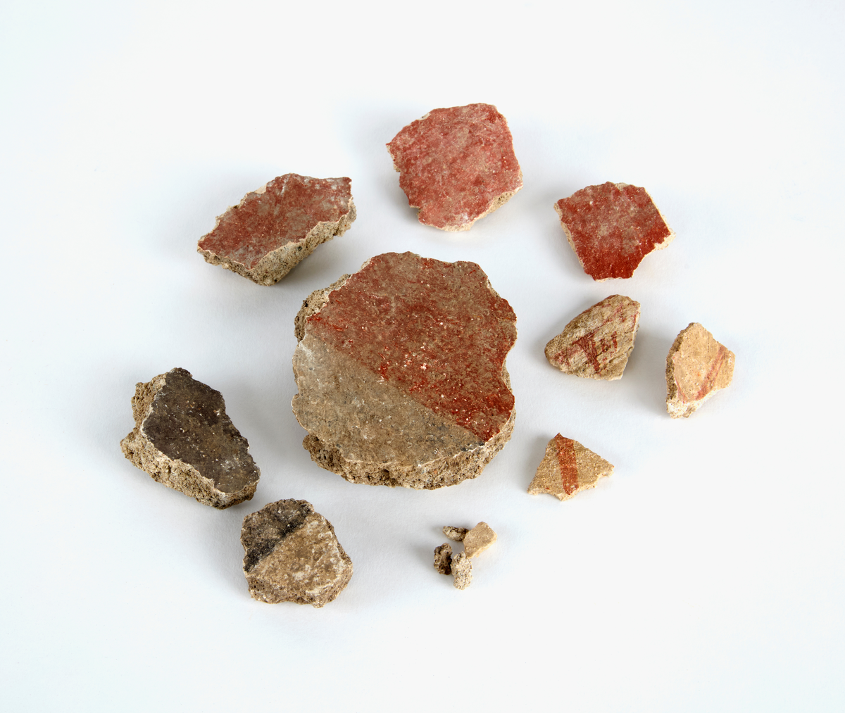 En samling av fragment av målad puts och bruk med kalkputs och bemålning. 17 fyndaskar med fragment i olika storlekar.

Fyndask 1: Totalt 13 fragment med röd och vit färg, en ser ut att ha träavtryck (varit fäst mot ett trästycke).

Fyndask 2: Totalt 7 fragment alla utom en har röd och vit färg, endast en med gråaktig obehandlad puts. 

Fyndask 3: Totalt 1 större fragment med röd och vit färg på enda sidan.

Fyndask 4: Totalt 4 fragment alla utom en med röd och vit färg, endast en med vit puts. 

Fyndask 5: Totalt 3 fragment med röd och vit färg, varav en är sotig. 

Fyndask 6: Totalt 3 fragment med röd och vit färg, en mycket tydlig medan de andra två mer diffusa. 

Fyndask 7:  Totalt 27 fragment, 24 av dessa är bemålade med röd och vit färg, 3  fragment med gråaktig obehandlad puts. 

Fyndask 8: Totalt 5 fragment, varav 4 större och en mycket liten. Alla större fragment med olika karaktär. En med vit kalkbruk och utan putsad yta, en annan med svart och röd putsad yta. Det tredje fragmentet har lite rödfärgad puts bevarad och på andra sidan ser det ut att ha träavtryck (varit fäst mot ett trästycke). Det fjärde fragmentet har en mer brungrå nyans. I fyndasken låg en lapp med text N. om V. portalen. 

Fyndask 9: Totalt 13 fragment, varav ett större fragment med svart och rödmålad puts. Ett annat fragment med svart och vitmålad puts, det tredje fragmentet har endast svartmålad puts. Sedan finns tre rödmålande putsfragment, samt tre fragment med röda linjer. Fyra fragment är ytterst små och intetsägande.

Fyndask 10: Totalt 9 fragment samt smådelar varav två har rött färgfragment. Det största fragmentet samt fyra andra är svart- och rödmålat. Tre putsfragment har röda linjer.
 
Fyndask 11: Totalt 1 fragment med röda linjer samt en mindre del med blågråa linjer. 

Fyndask 12: Totalt 1 fragment med blågrå rundad linje samt samt en mindre punkt eller koncentration nedanför.  

Fyndask 13: Totalt 5 fragment varav två med rödmålad puts. De andra tre har linjer. 

Fyndask 14: Totalt 1 fragment med vit och rödmålad puts, med flertal linjer som eventuellt kan vara del av en bokstav.
 
Fyndask 15: Totalt 1 fragment med vit och svartmålad puts, med flertal linjer som eventuellt kan vara del av en större figur. Ena delen syns en större koncentration som skulle kunna vara en fågel. 

Fyndask 16: Totalt 1 fragment med vit och rödmålad puts, med flertal rundade linjer som eventuellt kan vara del av växtlig dekor.

Fyndask 17: Totalt 1 fragment med rödmålad puts, med en vit linje.