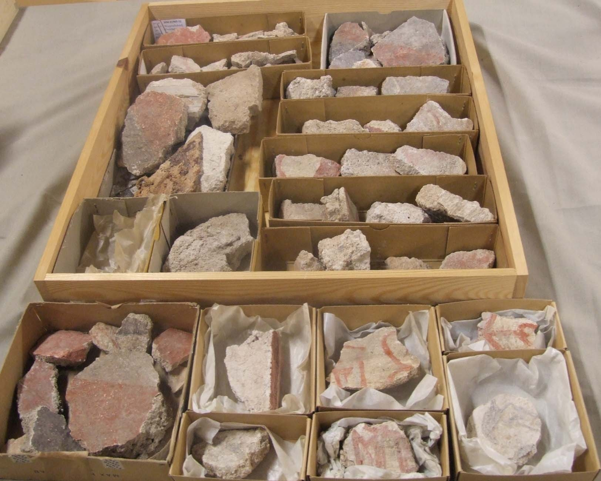 En samling av fragment av målad puts och bruk med kalkputs och bemålning. 17 fyndaskar med fragment i olika storlekar.

Fyndask 1: Totalt 13 fragment med röd och vit färg, en ser ut att ha träavtryck (varit fäst mot ett trästycke).

Fyndask 2: Totalt 7 fragment alla utom en har röd och vit färg, endast en med gråaktig obehandlad puts. 

Fyndask 3: Totalt 1 större fragment med röd och vit färg på enda sidan.

Fyndask 4: Totalt 4 fragment alla utom en med röd och vit färg, endast en med vit puts. 

Fyndask 5: Totalt 3 fragment med röd och vit färg, varav en är sotig. 

Fyndask 6: Totalt 3 fragment med röd och vit färg, en mycket tydlig medan de andra två mer diffusa. 

Fyndask 7:  Totalt 27 fragment, 24 av dessa är bemålade med röd och vit färg, 3  fragment med gråaktig obehandlad puts. 

Fyndask 8: Totalt 5 fragment, varav 4 större och en mycket liten. Alla större fragment med olika karaktär. En med vit kalkbruk och utan putsad yta, en annan med svart och röd putsad yta. Det tredje fragmentet har lite rödfärgad puts bevarad och på andra sidan ser det ut att ha träavtryck (varit fäst mot ett trästycke). Det fjärde fragmentet har en mer brungrå nyans. I fyndasken låg en lapp med text N. om V. portalen. 

Fyndask 9: Totalt 13 fragment, varav ett större fragment med svart och rödmålad puts. Ett annat fragment med svart och vitmålad puts, det tredje fragmentet har endast svartmålad puts. Sedan finns tre rödmålande putsfragment, samt tre fragment med röda linjer. Fyra fragment är ytterst små och intetsägande.

Fyndask 10: Totalt 9 fragment samt smådelar varav två har rött färgfragment. Det största fragmentet samt fyra andra är svart- och rödmålat. Tre putsfragment har röda linjer.
 
Fyndask 11: Totalt 1 fragment med röda linjer samt en mindre del med blågråa linjer. 

Fyndask 12: Totalt 1 fragment med blågrå rundad linje samt samt en mindre punkt eller koncentration nedanför.  

Fyndask 13: Totalt 5 fragment varav två med rödmålad puts. De andra tre har linjer. 

Fyndask 14: Totalt 1 fragment med vit och rödmålad puts, med flertal linjer som eventuellt kan vara del av en bokstav.
 
Fyndask 15: Totalt 1 fragment med vit och svartmålad puts, med flertal linjer som eventuellt kan vara del av en större figur. Ena delen syns en större koncentration som skulle kunna vara en fågel. 

Fyndask 16: Totalt 1 fragment med vit och rödmålad puts, med flertal rundade linjer som eventuellt kan vara del av växtlig dekor.

Fyndask 17: Totalt 1 fragment med rödmålad puts, med en vit linje.